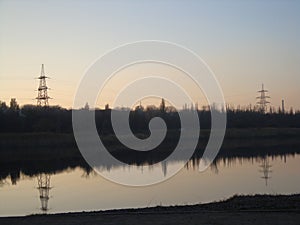 Poles with wires that transmit high-voltage current. Background of the evening sky with the sun