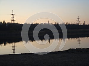 Poles with wires that transmit high-voltage current. Background of the evening sky with the sun