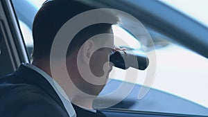 Police agent looking through binoculars from car, detective investigation, news