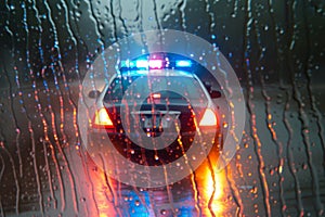 police car with strobes on, seen through a rainsoaked window