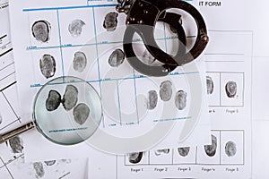 Police handcuffs and criminal fingerprints card, with magnifying glass, top view