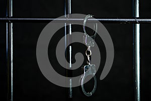 Police handcuffs are fastened to the bars of the cell for prisoners on a dark background, selective focus