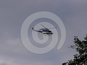 Police helicopter flying in the blue sky during the day, tree branches on the edges, close-up view