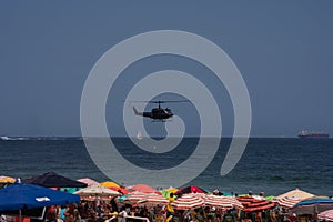 Police helicopter flying over crowded beach in Rio de Janeiro Brazil