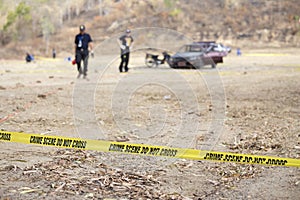 Police line tape with blurred law enforcement and wrecked car ba