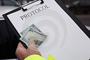 Police officer with bribe and clipboard near car outdoors, closeup