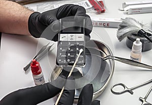 Police scientist takes DNA samples from phone involved in murder in lab, conceptual image