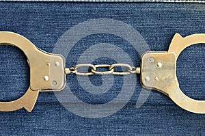 Police steel handcuffs lying on dark blue jeans background