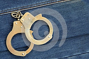 Police steel handcuffs lying on dark blue jeans background