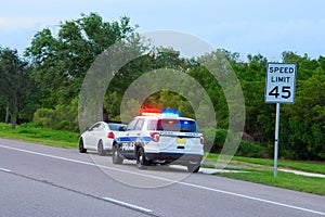 Police truck vehicle pulling over a sports car by speed limit sign