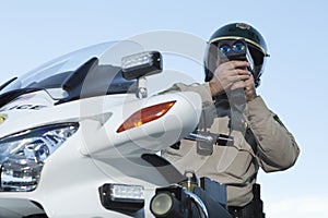 Policeman Monitoring Speed Through Radar Against Sky