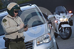 Policeman Writing Ticket While Standing In Front Of Car