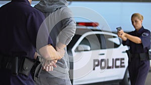 Policewoman aiming gun at criminal, male mate arresting hooligan, putting in car