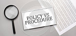 POLICY VS PROCEDURE sign in white paper notepad and magnifying glass on the grey background