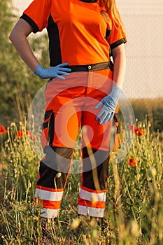 Polish ambulance worker standing in medical orange uniform with reflective elements and blue gloves on hands.