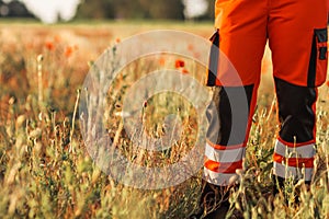 Polish ambulance worker standing in medical orange uniform with reflective elements. Poppy field background.