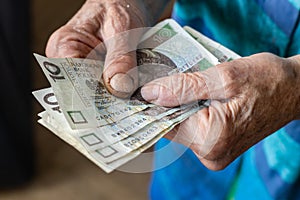 Polish pensioner holds several low-denomination banknotes in her hands, Cost of living of a senior citizen in Poland, Money Polish