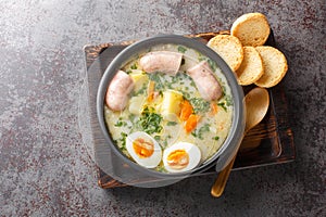 Polish Sour Rye Soup Zurek with white sausage, boiled egg and fresh veggies close-up in a bowl. Horizontal top view