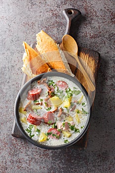 Polish white borscht with vegetables, smoked sausage, dried mushrooms and bacon close-up in a plate. Vertical top view