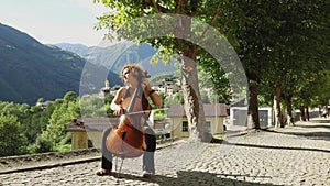 Polish woman and musician plays her cello sitting on a boulevard. Behind a valley in the middle of the Swiss