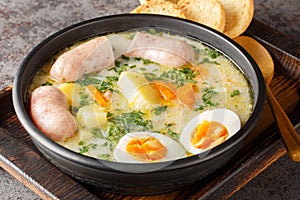 Polish zurek a rich soup soured with fermented rye starter, served with a boiled halved egg and a meaty white sausage close-up in