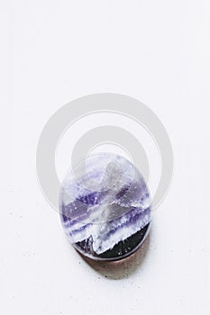 Polished amethyst tumbled stone pebble on a white background with empty space
