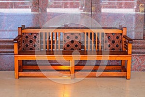 Polished luxurious wooden bench handmade  with a carved arabesque floral pattern against a pink brown marble wall