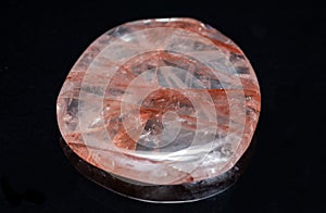 Polished quartz flat palm stone with red hematite inclusions from Madagascar isolated on black background