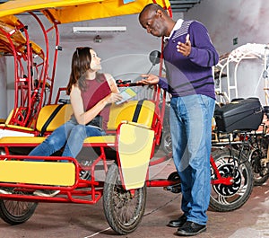 Polite African-American bikecab driver talking to young woman, offering rickshaw service photo