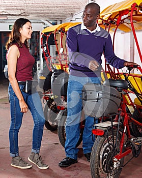 Polite African-American bikecab driver talking to young woman, offering rickshaw service photo