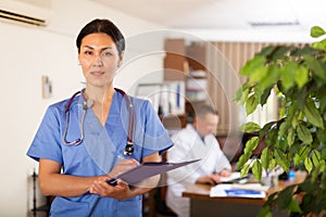 Polite Asian female doctor with clipboard meeting in clinic