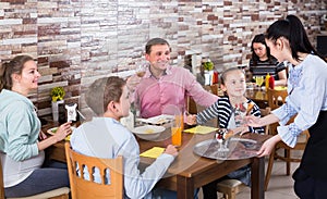 Polite professional waitress bringing ordered dishes to family