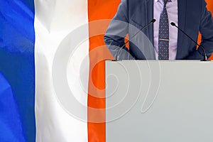 Political personality standing on the stage for conference on France flag background. Male speaker in France