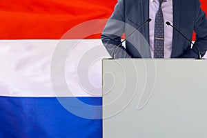 Political personality standing on the stage for conference on Netherlands flag background. Male speaker in Netherlands