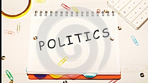 POLITICS word on a checkered notebook on a light table next to a magnifying glass, paper clips, stationery buttons, a calculator