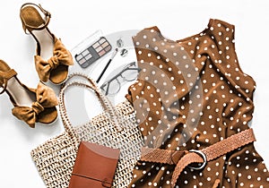 Polka dot summer brown dress, suede wedge sandals, eco straw tote bag, cosmetics on a light background, top view. Women`s clothin