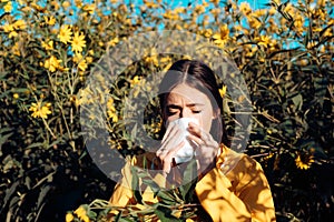 Pollen allergy concept. Young woman is going to sneeze. Closeup portrait of sneezing girl at yellow flowers background