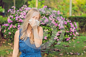 Pollen allergy concept. Young woman is going to sneeze. Flowering trees in background