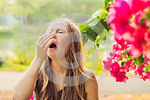 Pollen allergy concept. Young woman is going to sneeze. Flowering trees in background