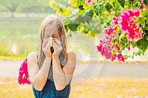 Pollen allergy concept. Young woman is going to sneeze. Flowering trees in background