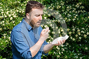 Pollen allergy in springtime concept. Man sneezing in a tissue