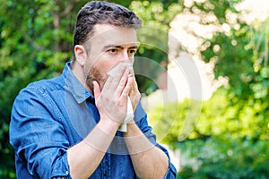 Pollen allergy in springtime concept. Man sneezing in a tissue