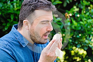 Pollen allergy in springtime concept. Man sneezing in a tissue