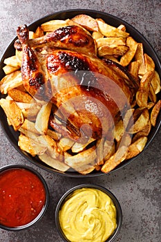 Pollo a la Brasa Peruvian Roast Chicken with fried potato and sauces closeup in the plate. Vertical top view photo