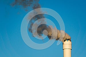 Polluted smoke against a clear blue sky from the tall chimney