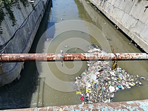 Polluted water and floating garbage flowing in the river under the bridge