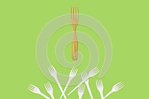 Polluting plastic forks and reusable wooden fork on a green background.