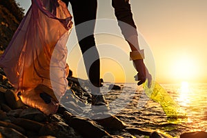 Pollution of ocean. A volunteer take a plastic bottle by the sea or river holding a plastic trash bag. Coastal cleanup