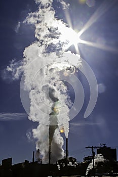 Pollution rises into the blue sky in front of a sun star