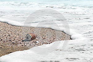 Pollution sea beach with metal waste. Single-use aluminum can on seashore discarded by ocean wave. Background Copy space